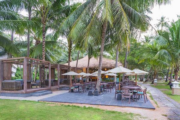 Außenbereich des Cape Panwa Hotels mit Tischen, Stühlen und Sonnenschirmen.