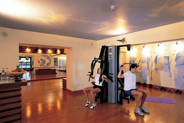 Fitnessbereich im Elounda Bay Palace mit zwei Personen, die an Fitnessgeräten trainieren.