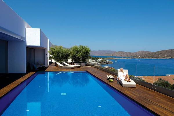 Person sitzt auf Liege am Pool mit Blick auf Meer und Berge, Elounda Bay Palace Hotel.
