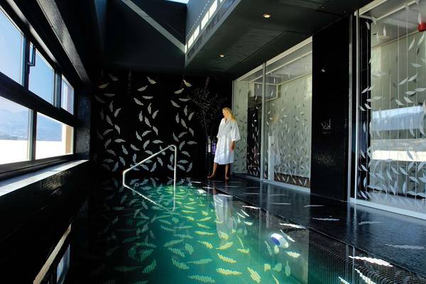 Eine Frau in einem weißen Bademantel steht am Rand eines grünen Pools im Elounda Bay Palace Hotel.