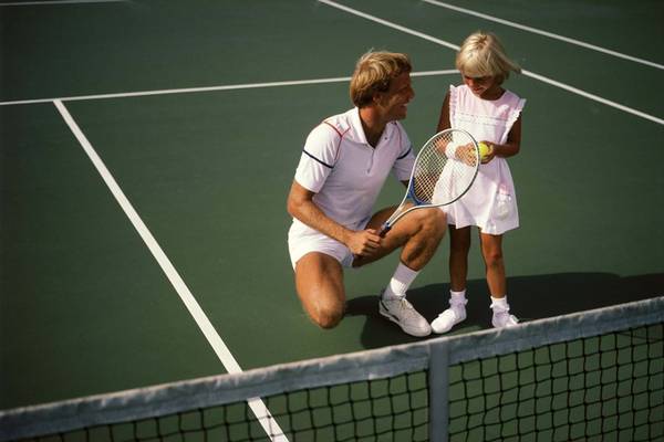 Ein Mann und ein Mädchen auf einem Tennisplatz, der Mann kniet und lächelt.