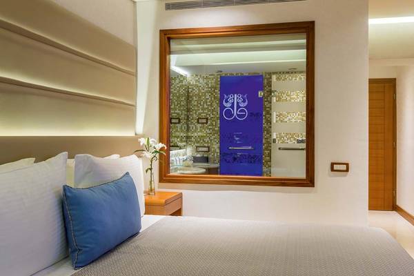Schlafzimmer im Elounda Bay Palace Hotel mit großem Bett, blauem Kissen und Fenster mit Spiegel