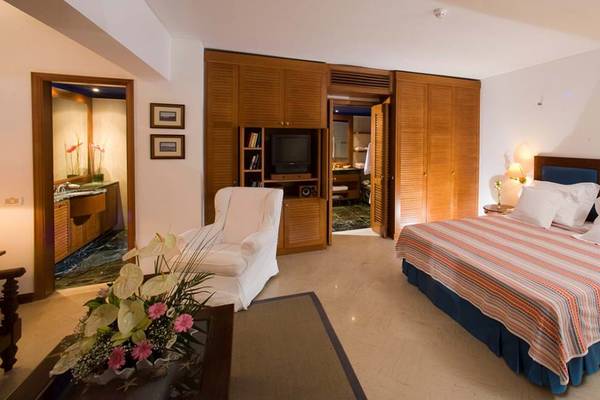 Schlafzimmer im Elounda Bay Palace Hotel mit Bett, Sessel, Fernseher und Holzschränken.