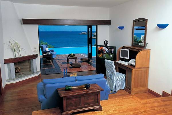Wohnzimmer mit Meerblick im Elounda Bay Palace Hotel, zeigt ein blaues Sofa, Fernseher und offene Terrassentüren.