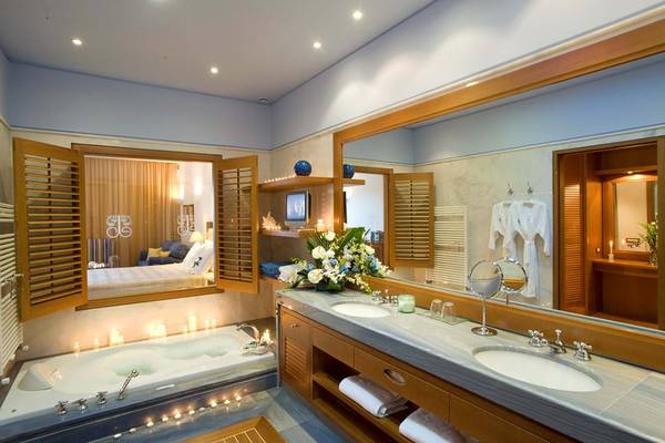 Badezimmer im Elounda Bay Palace Hotel mit Whirlpool und Blick auf das Bett.