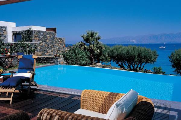 Außenpool des Elounda Bay Palace mit Blick auf das Meer und eine steinerne Mauer.
