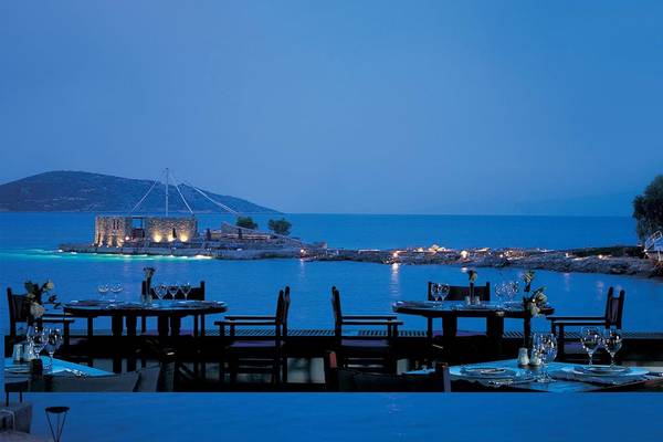 Außenbereich des Elounda Bay Palace Hotels mit Blick auf den Ozean und eine Insel bei Nacht.