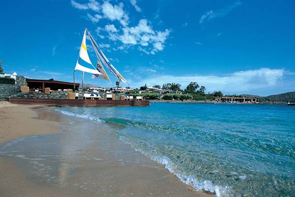 Elounda Bay Palace Hotel am Strand mit Segelboot und blauem Himmel
