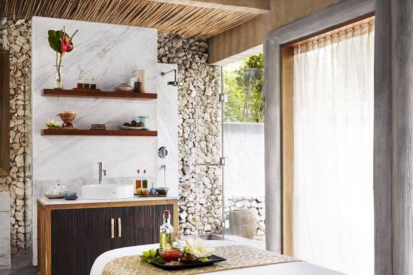 Badezimmer im Taj Coral Reef Resort & Spa mit Marmorwänden, offenem Duschbereich und einem Bett mit Pflegeutensilien.