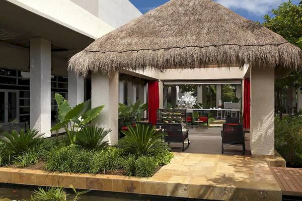 Außenbereich des Paradisus Playa del Carmen mit einer Strohdach-Hütte, Möbeln und Pflanzen.