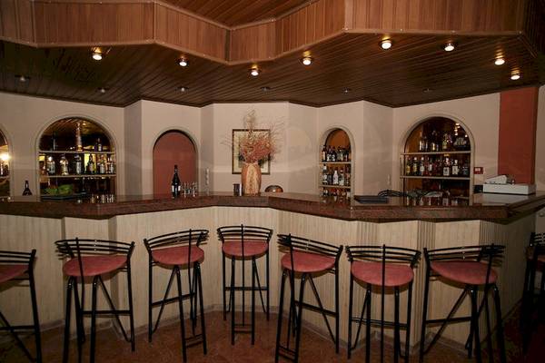 Barbereich des Paradise Hotel Corfu mit Holzdecken, Regalen voller Flaschen und geschwungenen Barhockern.
