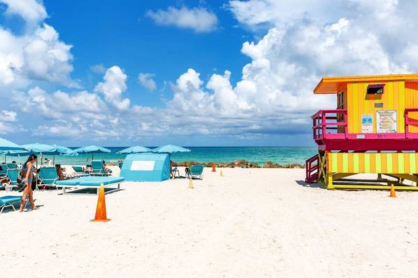 Ein Strand mit dem Palms Hotel und einer Rettungsstation, Sonnenschirme und Liegen sind aufgestellt.
