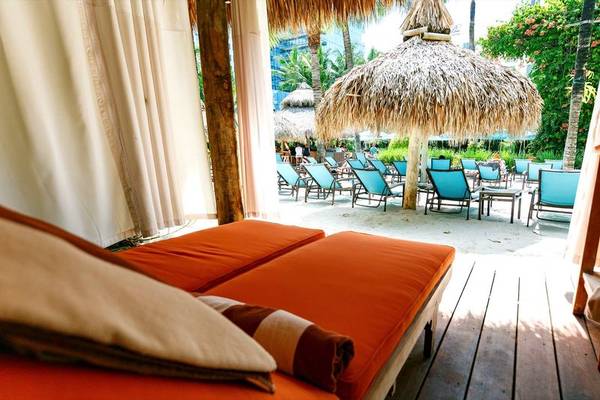 Oranges Sofa auf einer Holzterrasse im Palms Hotel & Spa mit Blick auf Lounge-Stühle und Sonnenschirme.