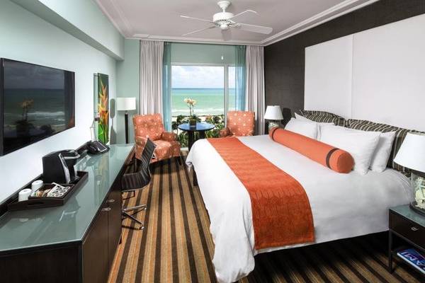 Innenansicht eines Zimmers im Palms Hotel & Spa mit Bett, Fernseher und Meerblick.