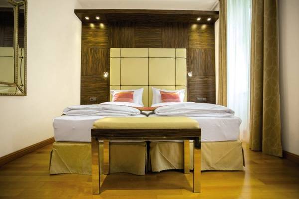Schlafzimmer im Best Western Plus Hotel mit einem großen Bett, Kopfteil, Nachttisch, Spiegel und goldenem Hocker.