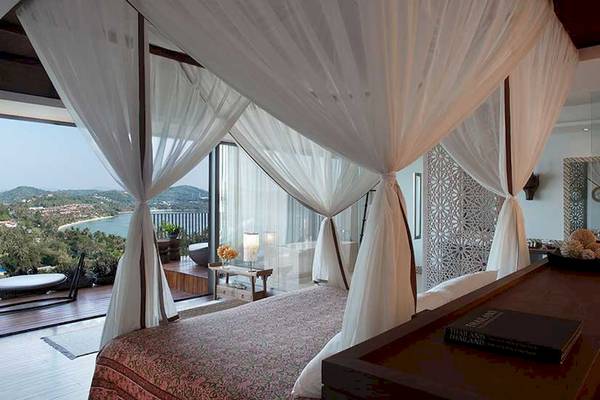 Schlafzimmer im Cape Panwa Hotel mit Bett, Vorhängen und Meerblick.