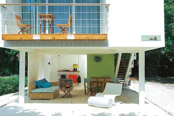 Ferienhaus mit Terrasse und Sandboden, Möbeln und Balkon mit Tisch und Stühlen.