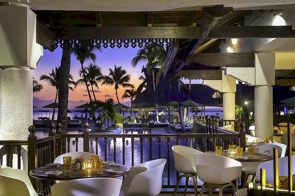 Terrasse des Sofitel Mauritius L'Imperial Resorts und Spa bei Sonnenuntergang mit Blick auf den Pool und die Palmen.