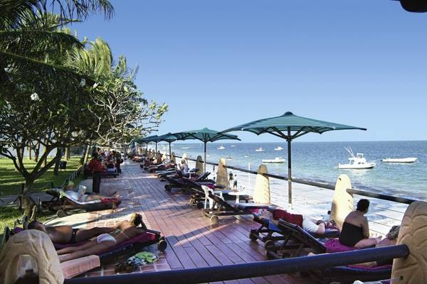 Besucher entspannen auf der Terrasse des Bamburi Beach Hotel mit Sonnenliegen und grünen Sonnenschirmen.