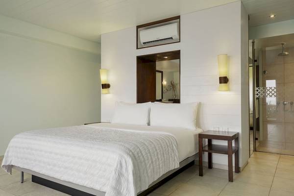 Ein modernes Hotelzimmer mit weißem Bett, Nachttischen und Dusche.