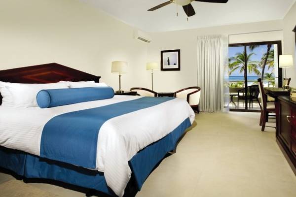 Ein geräumiges Hotelzimmer im Manchebo Beach Resort & Spa mit einem großen Bett und Blick auf das Meer.