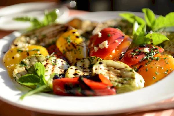 Ein Teller mit gegrilltem Gemüse, Tomaten und Basilikumblättern.