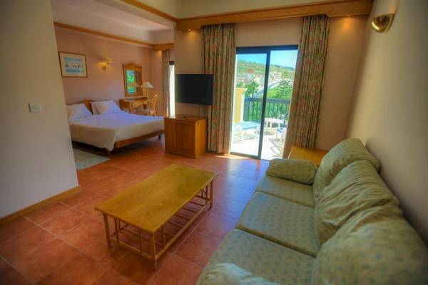 Innenansicht eines Zimmers im Saint Patrick's Hotel Gozo mit Bett, Couch, Tisch und Terrasse.