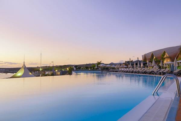 Außenpool des H10 Playa Meloneras Palace bei Sonnenuntergang mit Lounge-Stühlen und Palmen