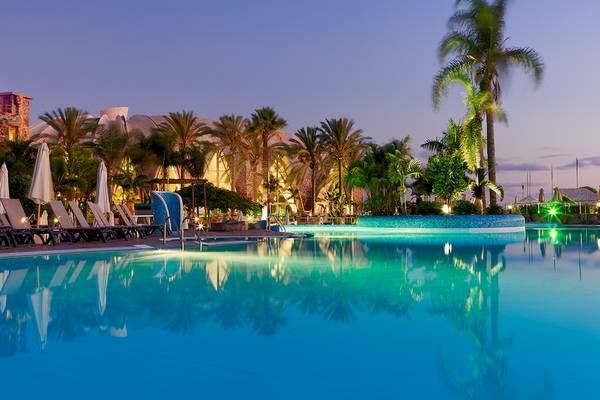 Außenpool des H10 Playa Meloneras Palace Hotels bei Nacht mit Palmen und Sonnenliegen.