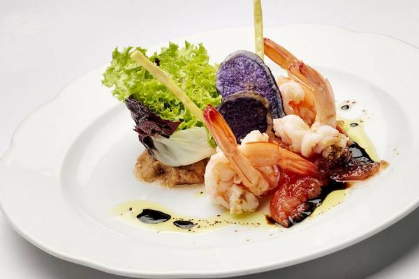 Elegantes Gericht mit Garnelen, Rotkohl und Beilagen auf einem weißen Teller.