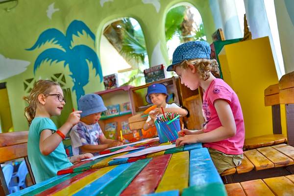 Vier Kinder sitzen am Tisch und schreiben im Kinderzimmer des Odyssee Resorts.