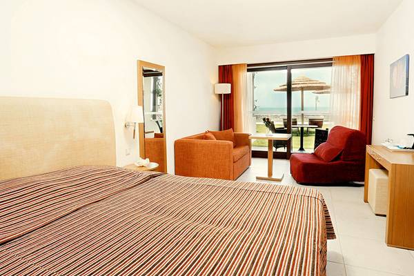 Innenansicht eines Zimmers im Blue Sea Beach Affiliated by Melia Hotel mit Bett, Sofas und Aussicht auf den Strand.