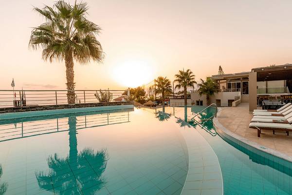 Ein Swimmingpool am Blue Sea Beach Hotel zur Sonnenuntergangszeit mit Palmen und einem Ausblick auf das Meer.