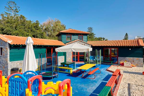 Spielplatz im Freien mit bunten Spielgeräten und Gebäuden im Hintergrund, Alexander Beach Hotel & Village Resort.
