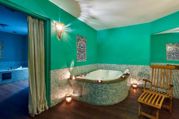 Badezimmer im Alexander Beach Hotel mit Badewanne, Holzstuhl und grünen Wänden.