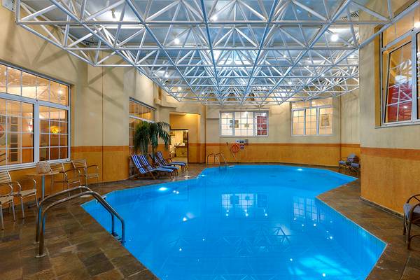 Ein Hallenbad im Alexander Beach Hotel mit Lounge-Stühlen und einer hohen Decke.