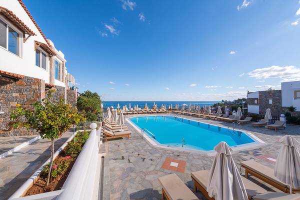 Außenpoolbereich des Alexander Beach Hotel & Village Resort mit Sonnenliegen und Blick auf das Meer.