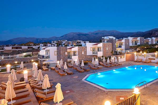 Alexander Beach Hotel & Village Resort Pool-Ansicht bei Nacht mit blauem Wasser, weißen Liegestühlen und abendlicher Beleuchtung.