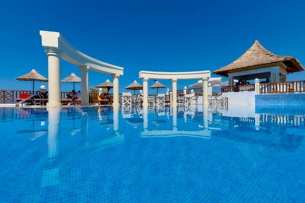 Außenpool des Alexander Beach Hotel mit weißen Säulen und Sonnenschirmen.