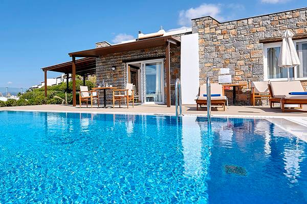 Poolseite des Alexander Beach Hotel & Village Resort mit Liegestühlen und Tisch.