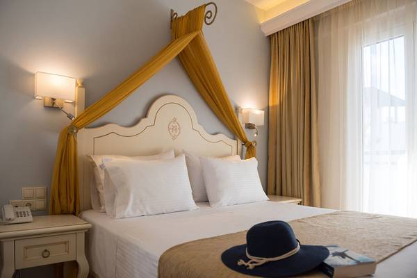 Schlafzimmer im Alexander Beach Hotel mit Bett, Kopfteil, Kissen und einer Mütze auf dem Bett.