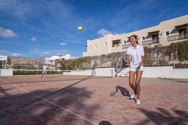 Tennisplatz im Alexander Beach Hotel & Village Resort mit einer Frau, die einen Ball schlägt.