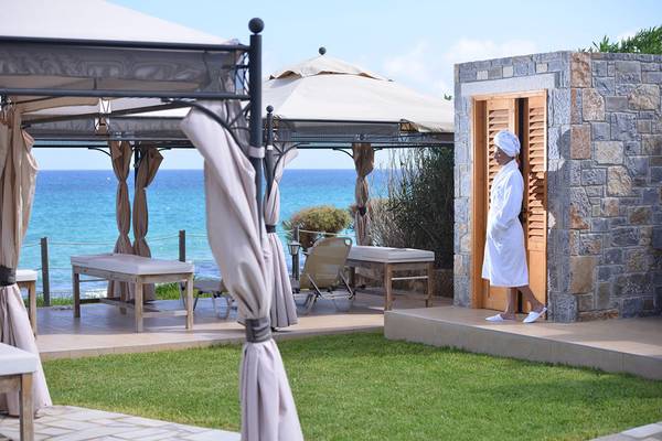 Frau im weißen Bademantel kommt aus einer Tür auf der Terrasse des Alexander Beach Hotel mit Blick auf das Meer.