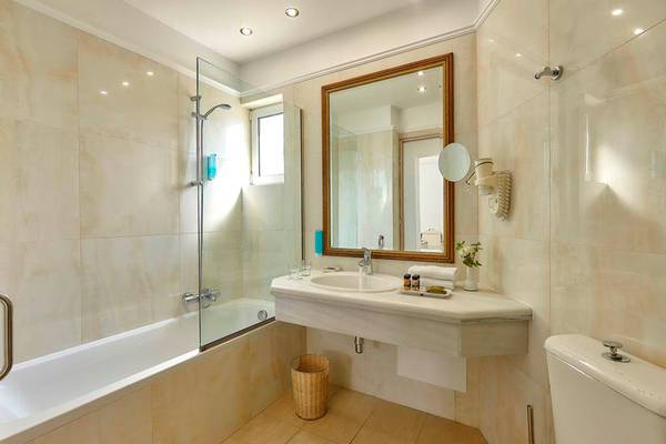Badezimmer im Alexander Beach Hotel mit Badewanne, Dusche, Spiegel und Toilette.