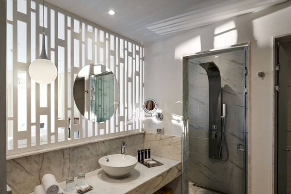 Innenansicht eines Badezimmers im Steigenberger Pure Lifestyle Hotel mit Marmorboden, Dusche, Waschbecken und Spiegel.