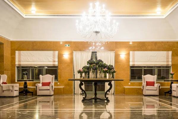 Empfangsbereich des Bella Beach Hotels mit einem großen Kronleuchter, weißen Sesseln und einem Tisch mit Blumen.