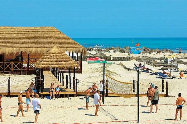 Leute spielen Volleyball auf einem Strand mit einem Gebäude mit Strohdach in der Nähe des Wassers.