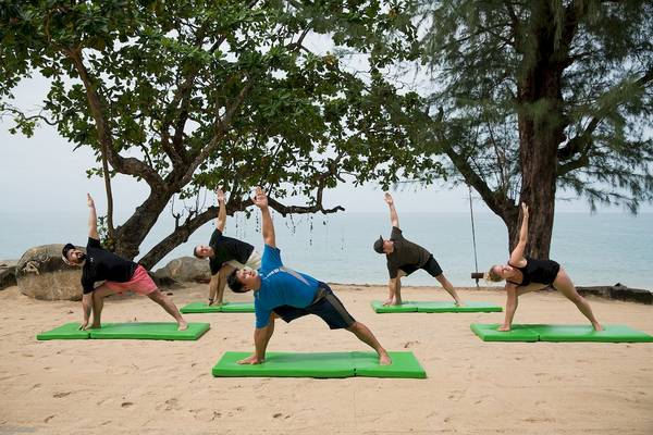 Gruppe von Menschen, die Yoga auf grünen Matten am Strand des Briza Beach Resorts praktizieren.