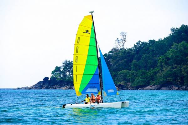 Drei Personen segeln auf einem bunten Segelboot auf dem Meer vor Kata Beach.
