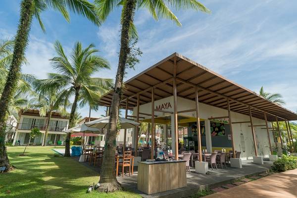 Außenbereich des Briza Beach Resorts mit Maya Cafe, Tischen und Stühlen unter Palmen.